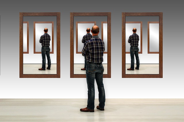 Ein Mann steht vor einer Wand mit drei Spiegeln.