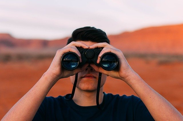 Mann mit Fernglas steht in der Wüste.